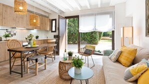 A modern kitchen with wooden cabinets, a dining area with a wooden table and chairs, and a cozy living room with a sofa and cushions. - Sant Mori- La Escala Boutique Apartment (Sant Mori)
