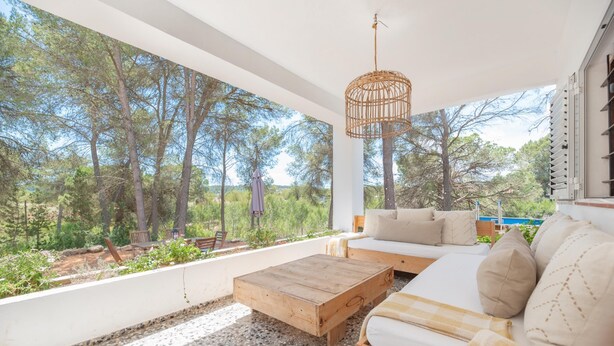 A modern outdoor living area with a wooden coffee table, a sofa with cushions, and a wicker hanging light fixture. - Can Vert - Casa Rural Ideal Para Desconectar (Santa Eulalia del Rio)