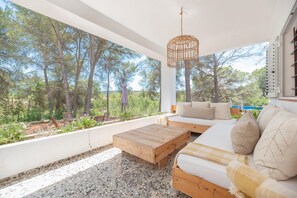 A modern outdoor living area with a wooden coffee table, a sofa with cushions, and a wicker hanging light fixture. - Can Vert - Casa Rural Ideal Para Desconectar (Santa Eulalia del Rio)