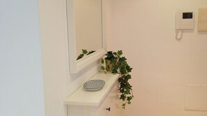 Un baño con tocador blanco, espejo, una planta pequeña, teléfono y toallero.