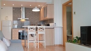 Un espacio habitable pequeño con kitchenette, un sofá gris y un televisor.