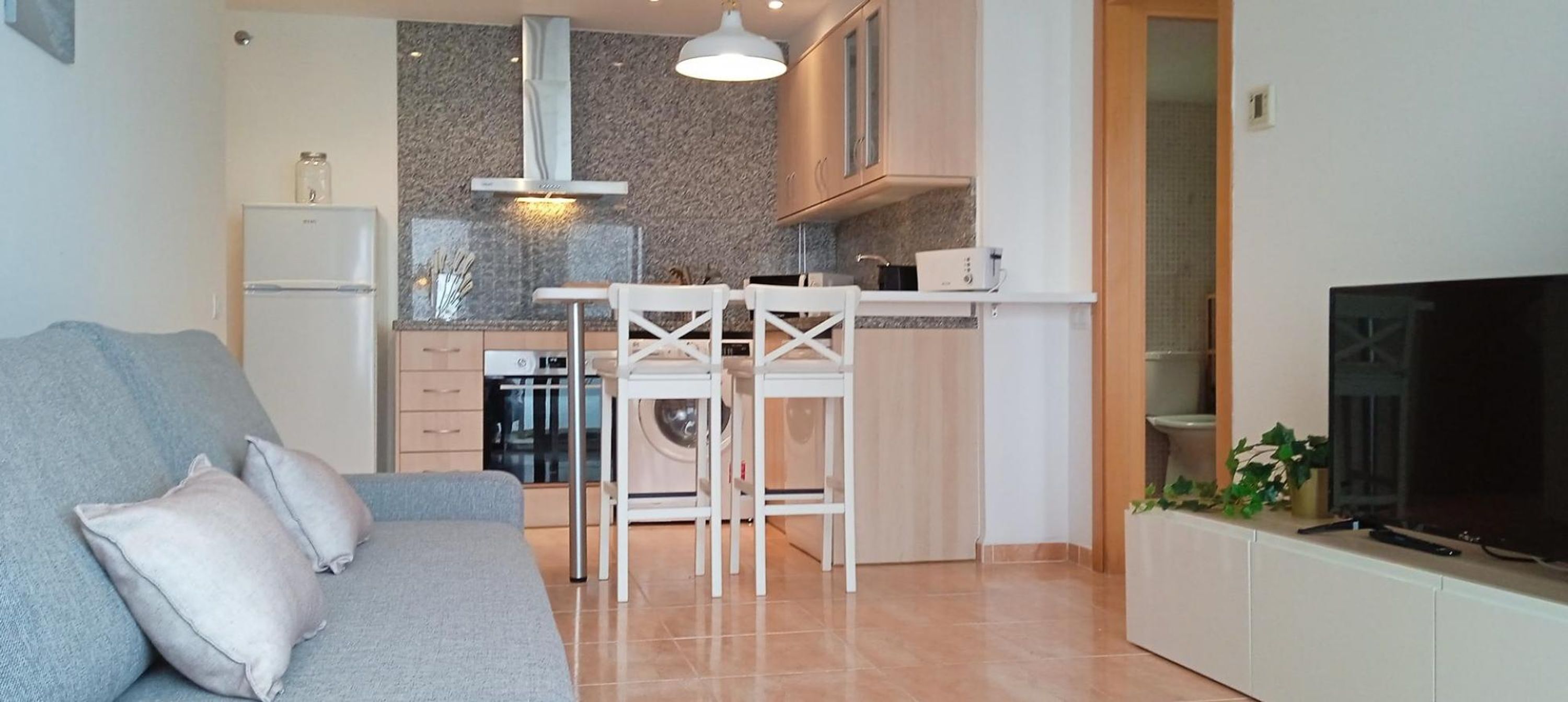 A compact living space with a sofa, a dining area with chairs, a kitchen with appliances, and a TV.