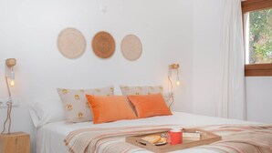 A neatly made bed with patterned pillows, a bedside table with a lamp, and a window with curtains. - Villa Sa Planeta in Sant Josep de Sa Talaia (Sant Josep de sa Talaia)
