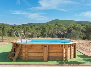 A wooden hot tub with two metal ladders on a green lawn, surrounded by a fence and trees, with a mountainous backdrop. - Villa Sa Planeta in Sant Josep de Sa Talaia (Sant Josep de sa Talaia)