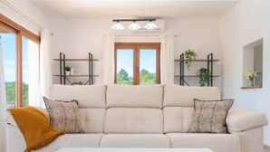 A modern living room with a beige sofa, two side tables, a wooden coffee table, and a view of greenery outside. - Villa Sa Planeta in Sant Josep de Sa Talaia (Sant Josep de sa Talaia)