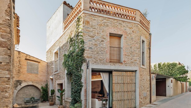 Un bâtiment en pierre doté d’un balcon en bois, d’une porte-fenêtre coulissante et d’un petit espace extérieur aménagé avec une table et des chaises.