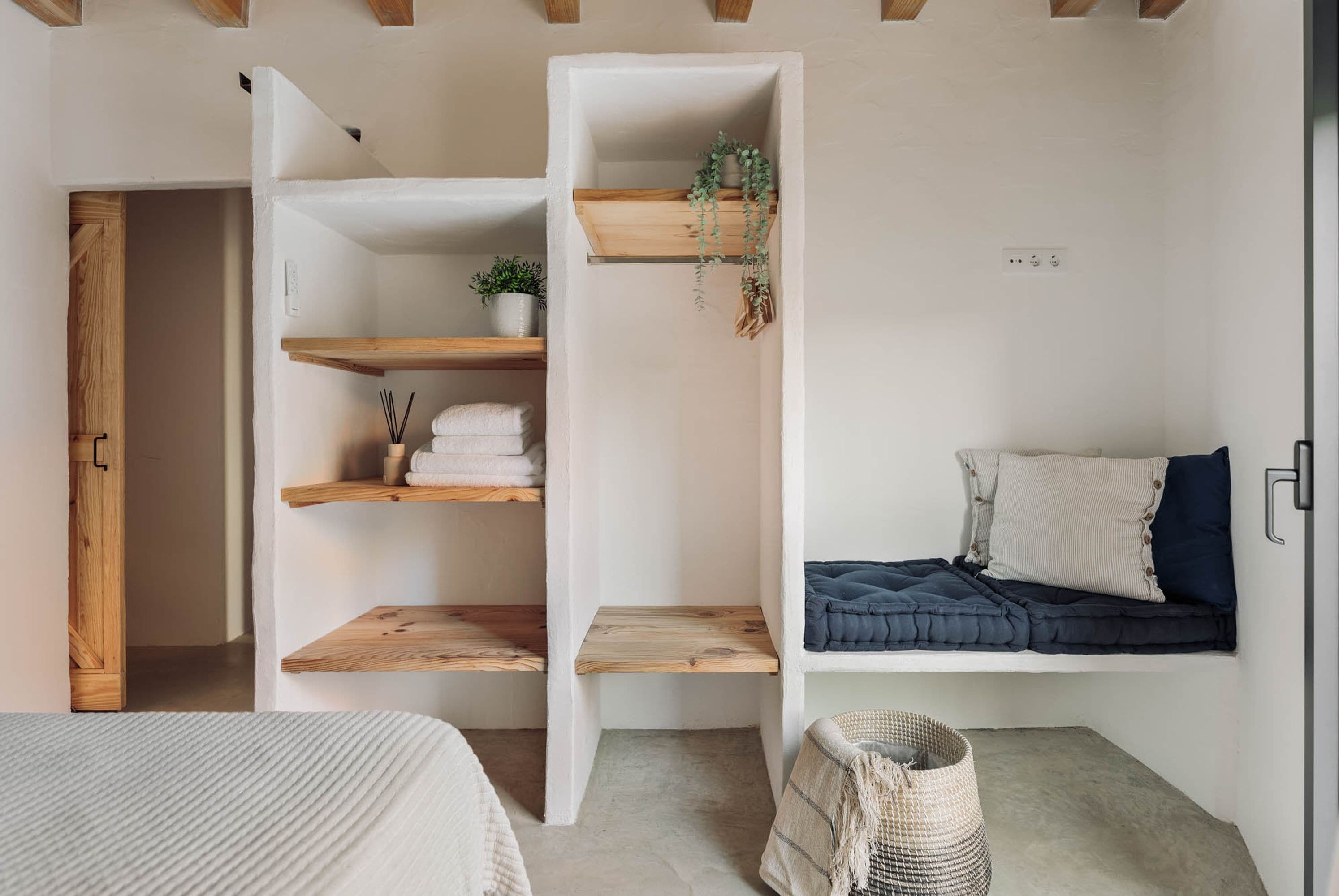 A bedroom with a bed, a built-in shelf unit with towels and plants, and a hanging plant.