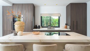 A modern kitchen with a marble countertop, dark wood cabinets, and a large window with a view of greenery. - Can Palau in Santa Eul ria des Riu (Santa Eulalia del Rio)