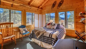 Un dormitorio de cabaña acogedor, con cama, una silla y ventanas amplias que dan al bosque.