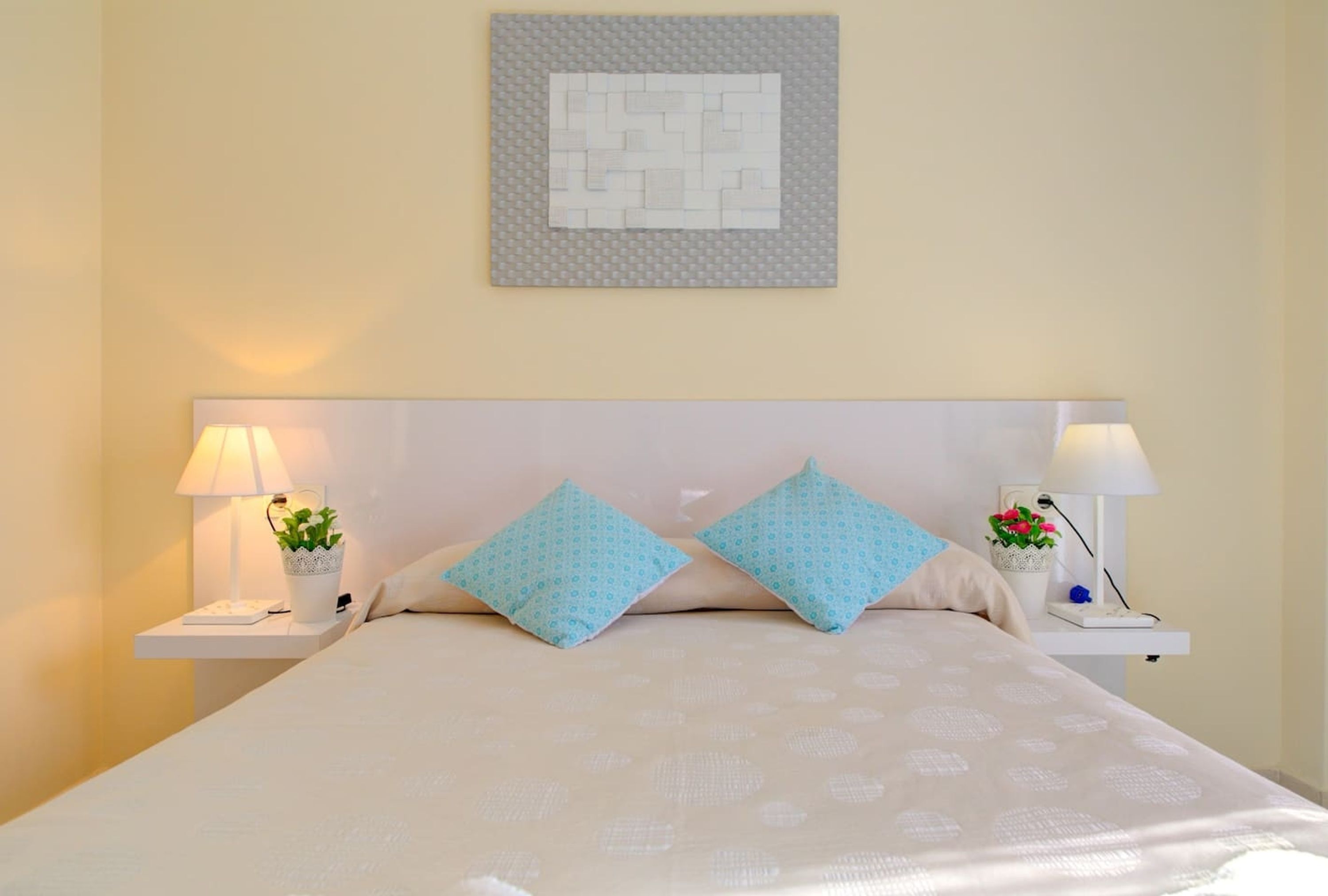 Un lit bien fait, recouvert d’une couvre-lit à motifs, avec deux oreillers assortis, deux tables de chevet dotées de lampes et une œuvre d’art accrochée au mur.