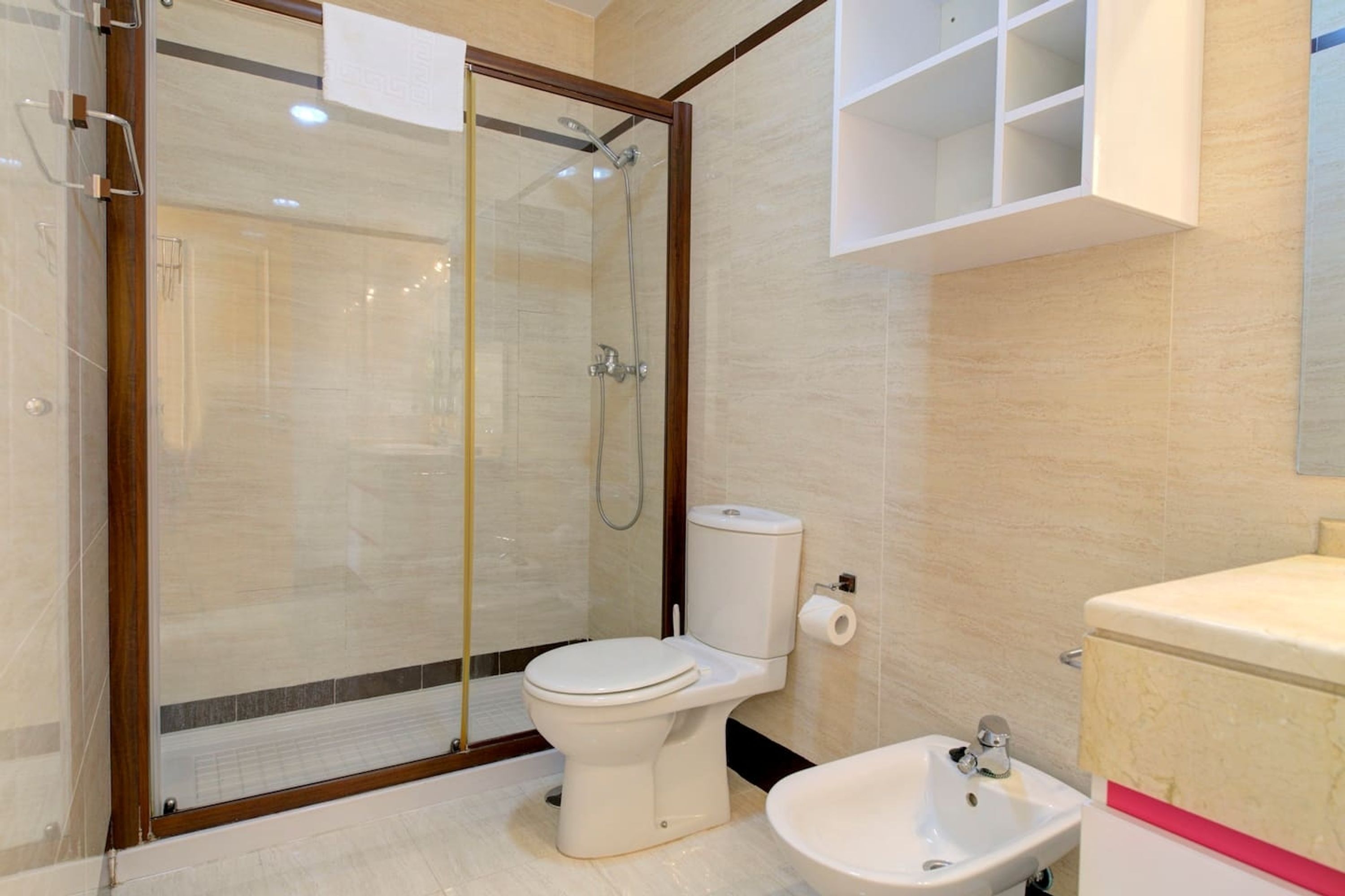 A modern bathroom with a glass-enclosed shower, a toilet, a bidet, and a sink.