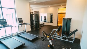 Une salle de sport équipée de tapis de course, d’un vélo elliptique, d’une machine de musculation et d’un miroir.