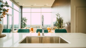 Une cuisine moderne dotée d’un grand îlot central, d’un évier en acier inoxydable et offrant une vue sur la ville grâce à de grandes fenêtres.