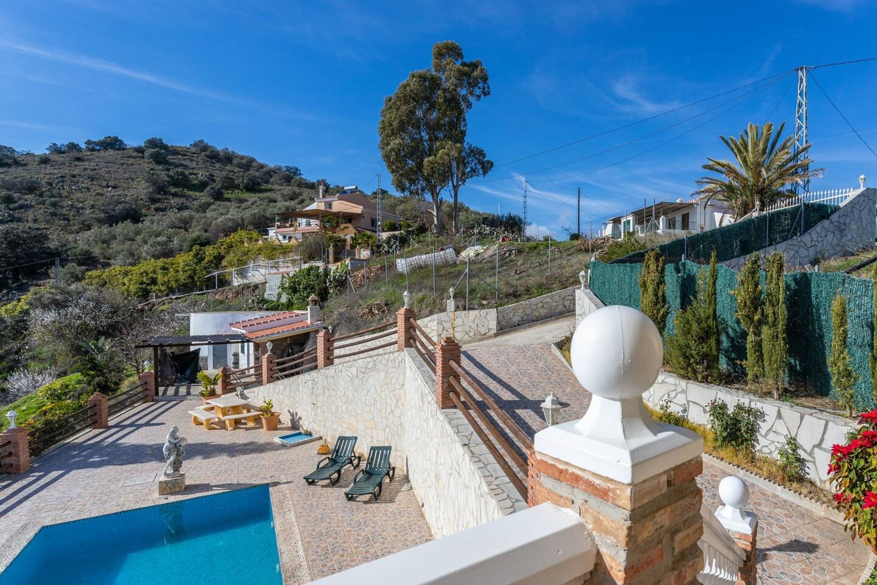 A pool area with lounge chairs, a statue, and a view of houses on a hillside.