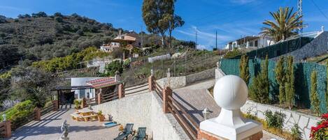A pool area with lounge chairs, a statue, and a view of houses on a hillside.