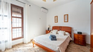 A bedroom with a wooden bed, a nightstand, a dresser, and a window with curtains. - Villa El Retiro in Frigiliana (Torrox)