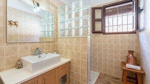 A bathroom with a large mirror, a sink, a shower, and a window with blinds. - Villa El Retiro in Frigiliana (Torrox)