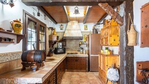 A rustic kitchen with wooden cabinets, a tiled backsplash, and a hanging pot rack. - Villa Mediterraneo Villa Mediterraneo Solset (Torrox)