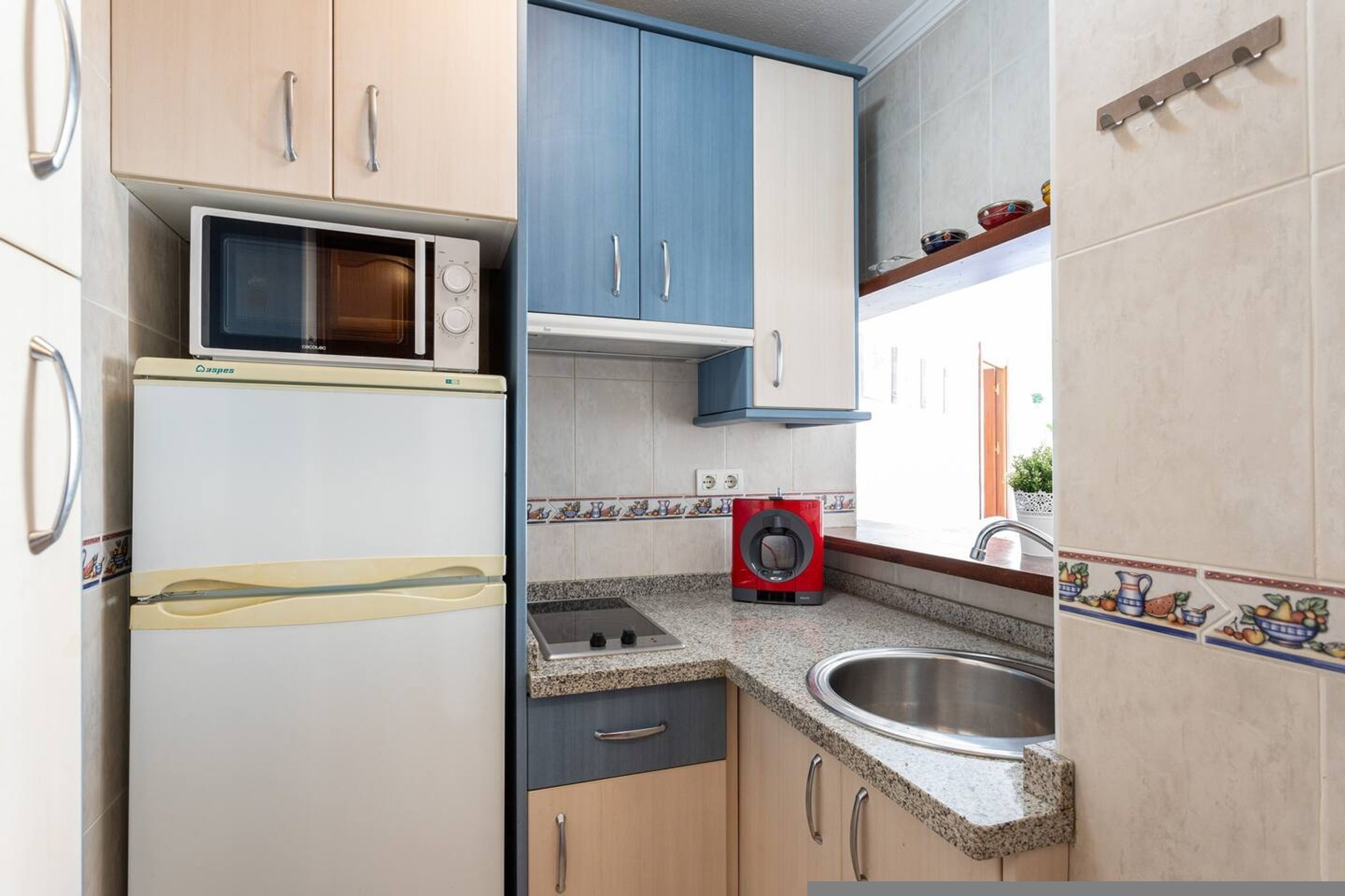 Une cuisine compacte équipée d’un four à micro-ondes, d’une petite cuisinière, d’un évier et d’un lave-linge rouge.