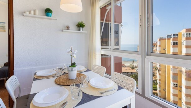 A dining area with a table set for four, a hanging pendant light, and a view of the sea through large windows. - Apartamento Torrox Playa Solset (Torrox)