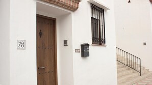 Un edificio blanco con puerta de madera, buzón y ventana con barrotes.