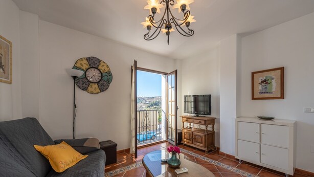 Una sala de estar con un sofá, una mesa de centro, un televisor, un armario y vistas a través de un ventanal.