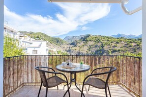 A balcony with wicker chairs and a glass table, overlooking a mountainous landscape. - Apartamento Alberti Solset (Frigiliana)