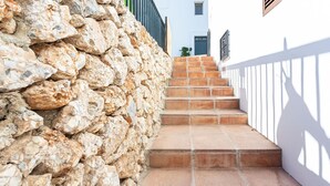 A stone wall adjacent to a set of terracotta-tiled stairs leading to a white building with a green door. - Apartamento Alberti Solset (Frigiliana)