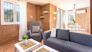 A cozy living room with a brick wall, a grey sofa, a white coffee table, and a grey armchair. - Apartamento Alberti Solset (Frigiliana)