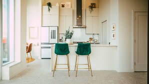 A modern kitchen with white cabinets, a central island, and two green velvet bar stools. - 902 (Halifax)