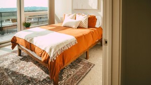A bedroom with a large bed, a view of the city, and a small plant on the windowsill. - 902 (Halifax)
