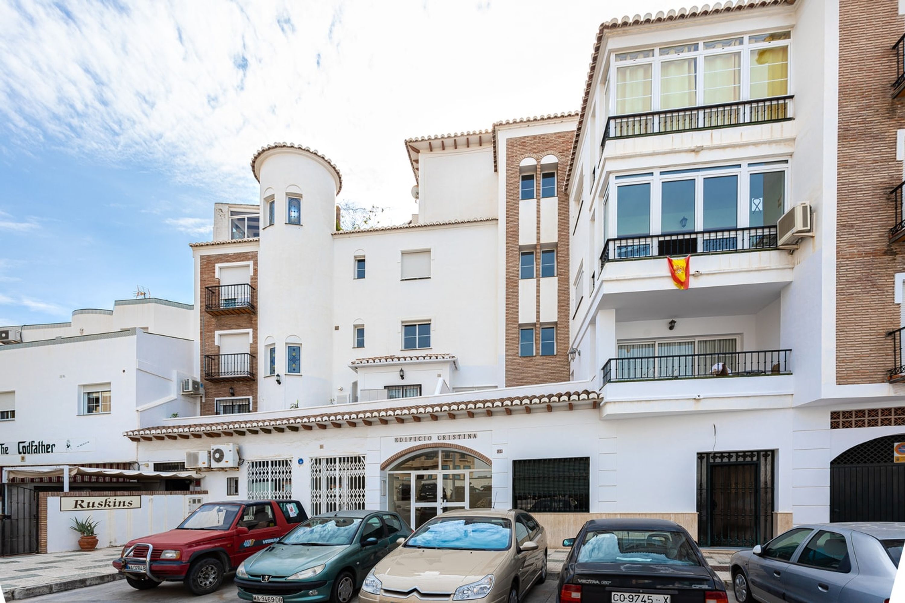 A multi-story building with a central entrance, balconies, and a clear sky.