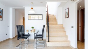 A modern interior with a staircase, two black leather chairs, a small table with a plant, and a pendant light.