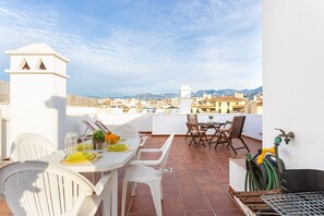 A terrace with a table set for dining, chairs, and a garden hose.