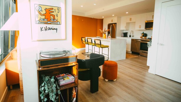 A modern kitchen with white cabinets, a central island, and a dining area with chairs. - Ph-2e (Halifax)