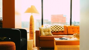 A modern living room with a sofa, armchair, and coffee table, large windows with a city view, and a tall floor lamp. - Ph-2e (Halifax)