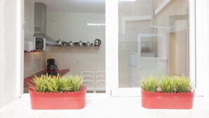 Una cocina moderna con armarios blancos, un microondas, una cafetera y una olla roja sobre la encimera. Hay dos macetas rojas en el alféizar de la ventana.