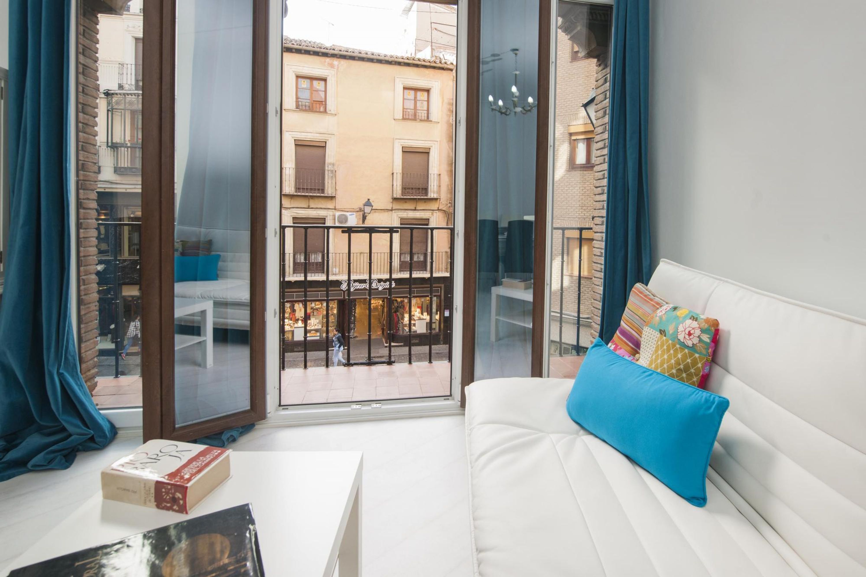 Una habitación con un sofá blanco, una mesita y un balcón con vistas a edificios.