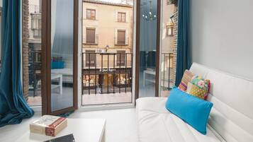 Una habitación con un sofá blanco, una mesita y un balcón con vistas a edificios.