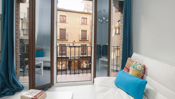Una habitación con un sofá blanco, una mesita y un balcón con vistas a edificios.