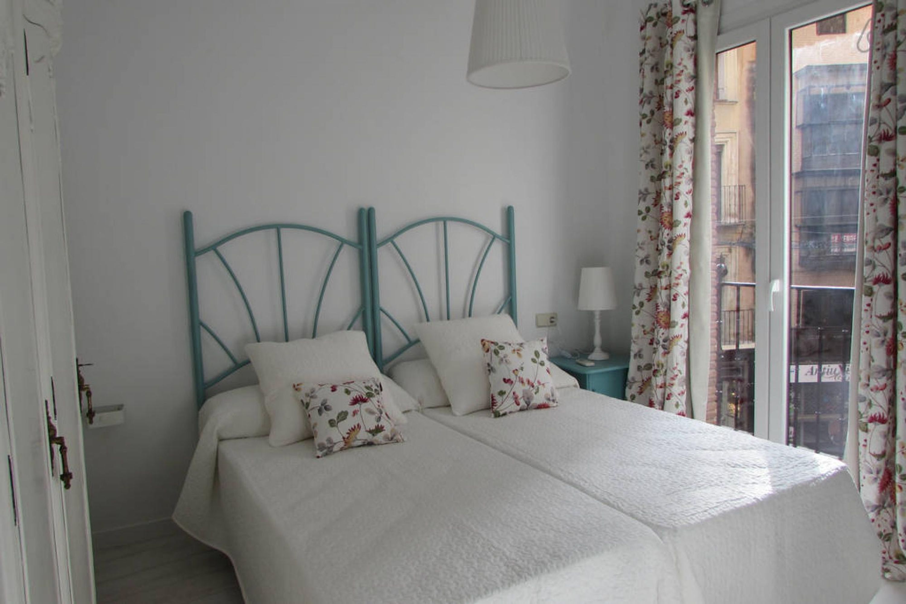Un dormitorio con cama, cortinas florales y vistas a edificios.