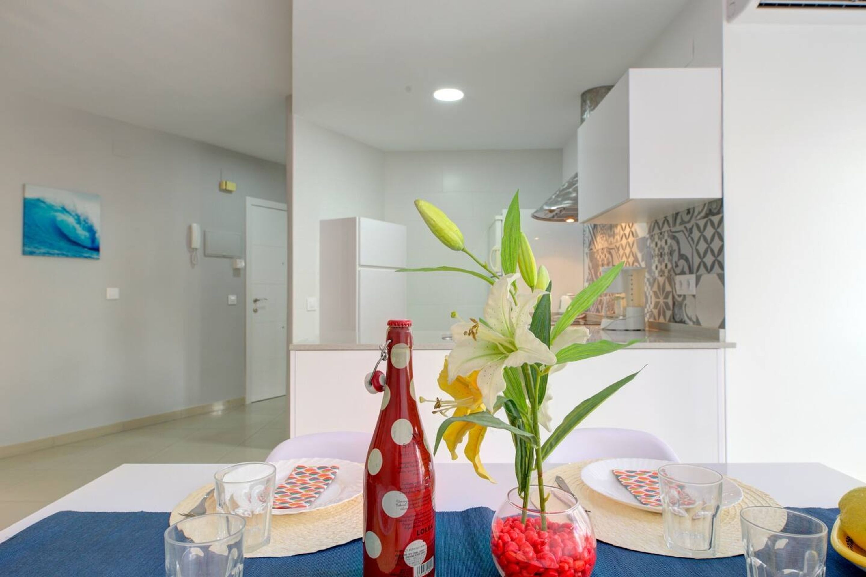 Una mesa de comedor con una botella, vasos y un florero con flores.