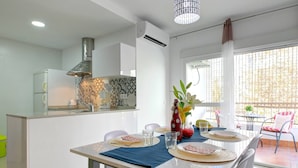 A modern kitchen with a central island, a dining area with a table set for two, and a view of the outside balcony. - Apartamento Palmeras 29 Solset (Nerja)