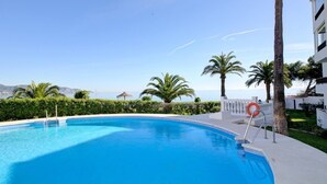 A clear blue pool with a lifebuoy, surrounded by palm trees and a view of the sea. - Apartamento Palmeras 29 Solset (Nerja)