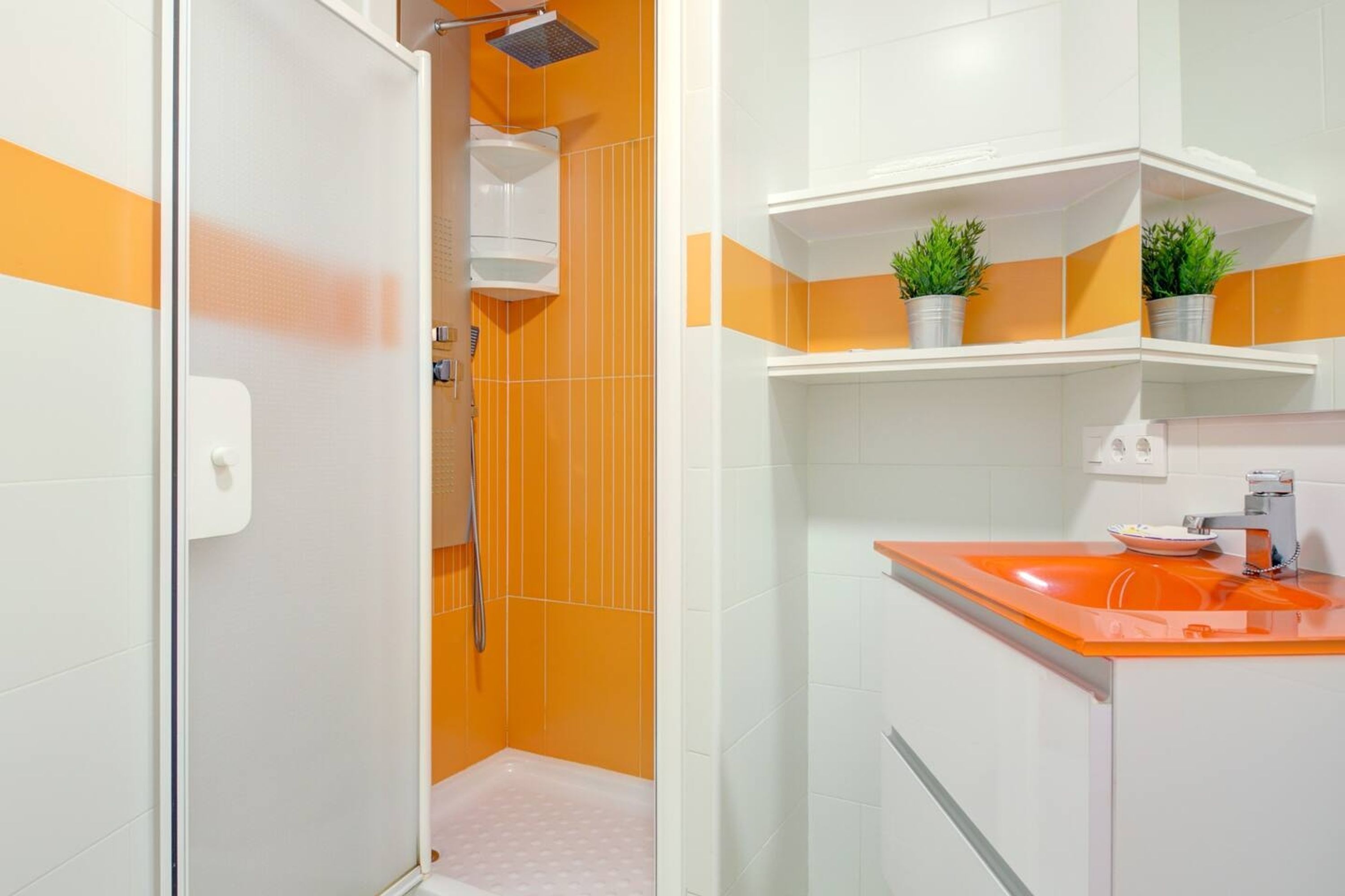 A bathroom with a shower, a sink with a mirror, and shelves with potted plants.
