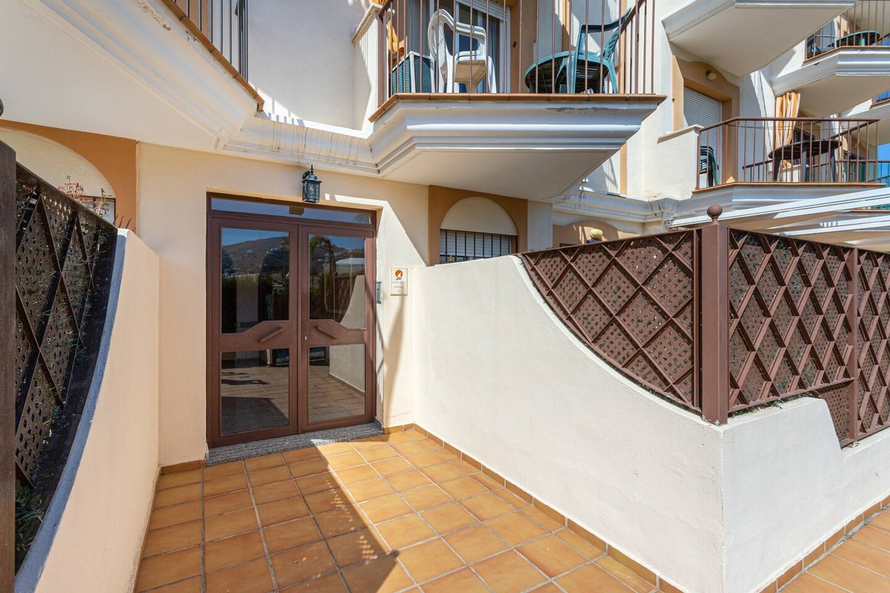 A residential building with a gated entrance, a balcony with outdoor furniture, and a tiled patio area.