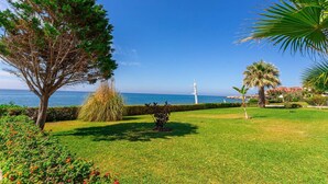 Un jardín cuidado con diferentes árboles y arbustos, una vista despejada del mar y un faro a lo lejos.