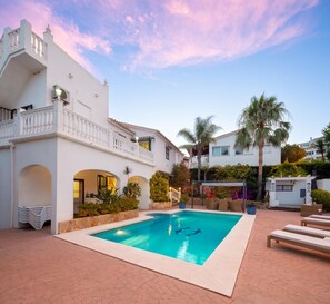 Ein Swimmingpool, umgeben von einem weißen Gebäude mit Balkon, Palmen und Sitzgelegenheiten im Freien.