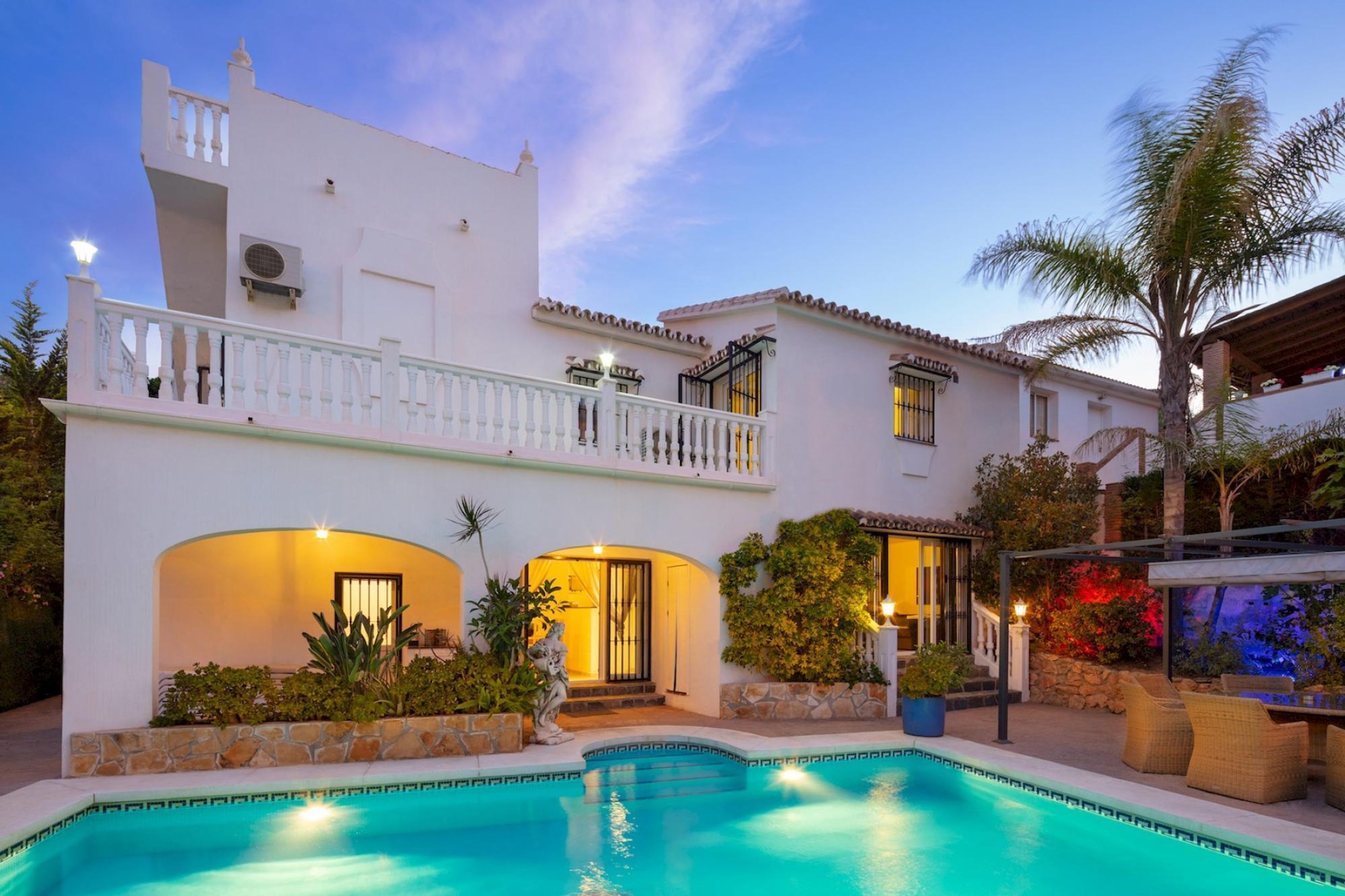 Un edificio blanco de dos pisos con piscina, mobiliario exterior y un patio cubierto.