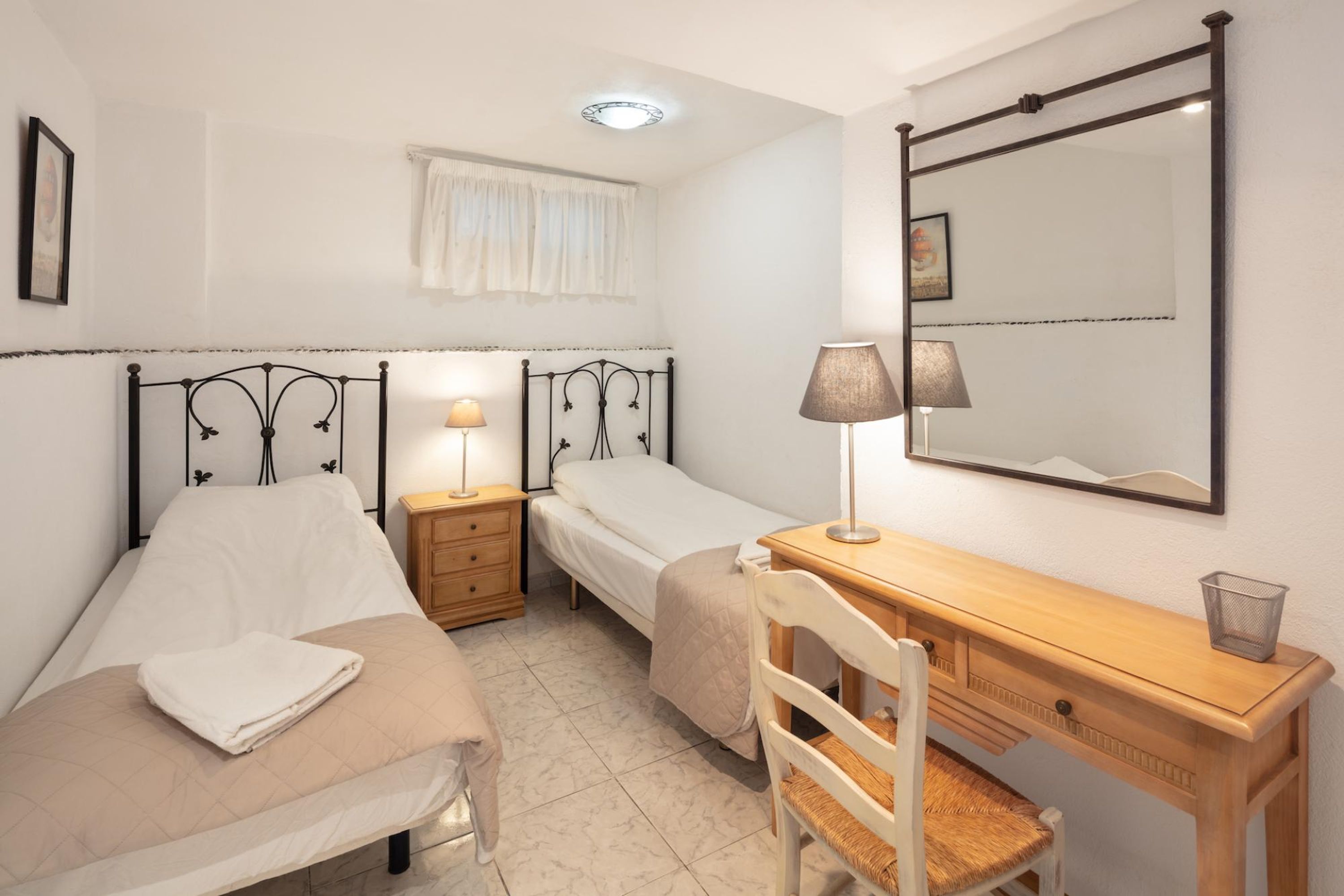 Ein Schlafzimmer mit zwei Einzelbetten, einem Holztisch, einem Stuhl, einem Spiegel und Nachttischen mit Lampen.